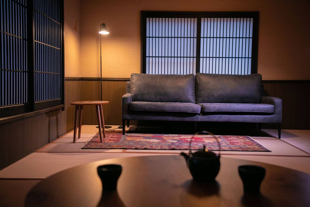 A room with a sofa, a small stool, a table with a teapot, and a floor mat.