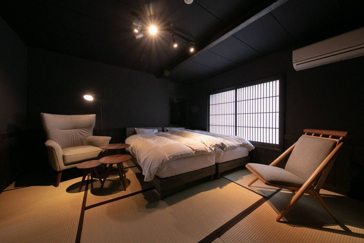 A room with a bed, two chairs, a small table, and a window with bars.