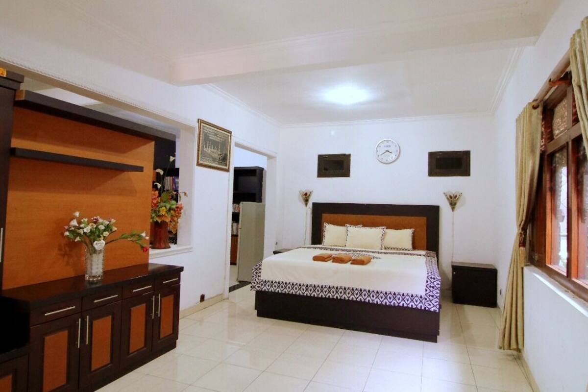 A bedroom with a bed, a dresser, a clock, and a window with curtains.