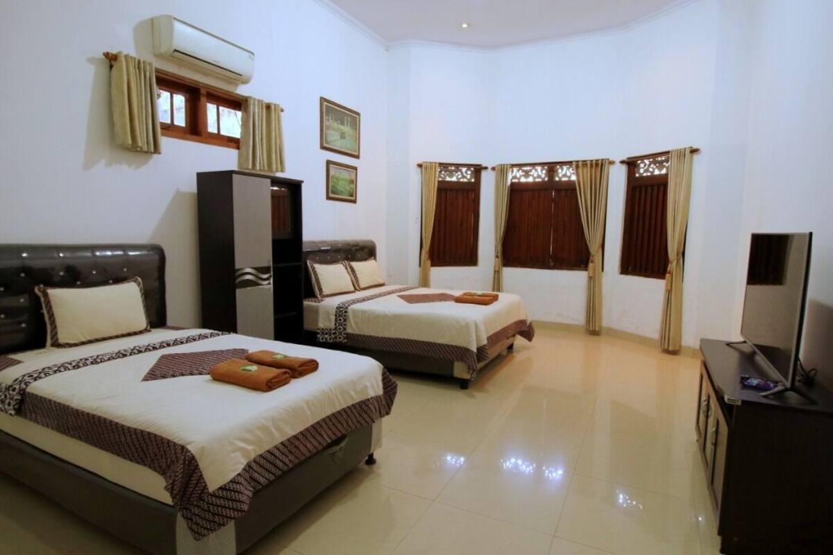 A hotel room with two beds, a TV, and an air conditioning unit.