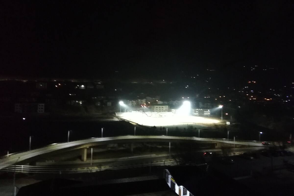 Vista nocturna de un puente con farolas y edificios al fondo.
