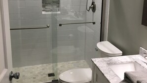 Ein modernes Badezimmer mit einer Glaskabine zur Dusche, Toilette und Waschbecken mit Marmorplatte.