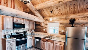 A rustic kitchen with wooden walls, a stainless steel refrigerator, a microwave, a stove, and a sink.
