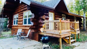 A log cabin with a deck, outdoor seating, and a barbecue grill.