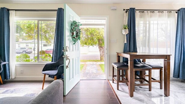 Una habitación con una mesa de comedor, dos sillas, un sofá y una puerta que da al exterior.