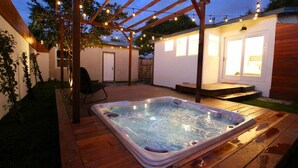Un jacuzzi en una terraza de madera con pérgola y luces colgantes.