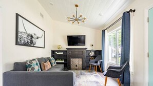 Una sala de estar moderna con un sofá gris, chimenea, televisor y un amplio ventanal con cortinas.