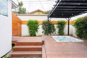 A wooden deck with a hot tub, surrounded by a white wall with wooden accents and green plants.