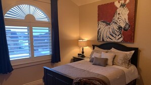A bedroom with a bed, a zebra painting, a lamp, and a window with blinds.