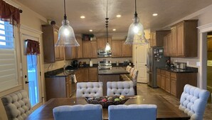 A spacious kitchen with a central island, pendant lighting, and a dining area with a wooden table and upholstered chairs.