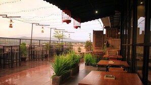 Un patio al aire libre con mesas y sillas, luces colgantes y plantas en macetas.