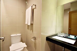 A modern bathroom with a toilet, a sink with toiletries, and a mirror. - Hotel Agria Bogor - Tajur (Bogor)