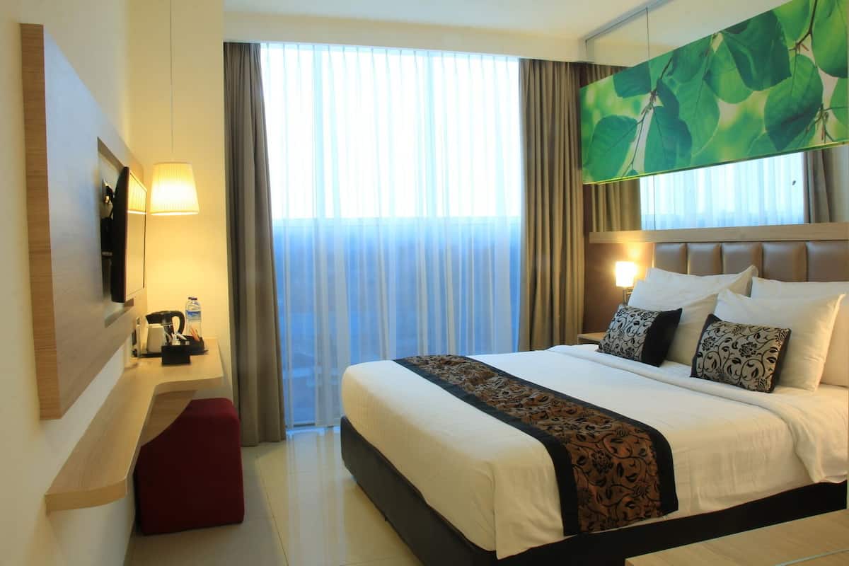 Een hotelkamer met een groot bed, een flatscreen televisie aan de muur, een bureau met een lamp en een raam met dunne gordijnen.