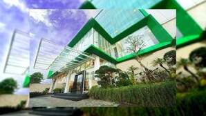Un edificio moderno con fachada de vidrio y detalles verdes, que incluye una entrada cubierta y un jardín bien cuidado.