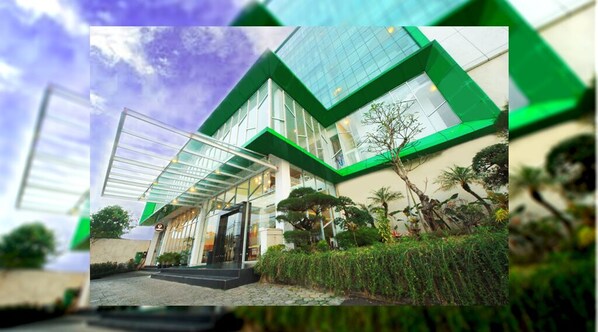 A modern building with a glass facade and green accents, featuring a covered entrance and a well-maintained garden. - Hotel Agria Bogor - Tajur (Bogor)