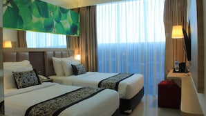 Habitación de hotel con dos camas, televisión, escritorio y un ventanal grande con cortinas.