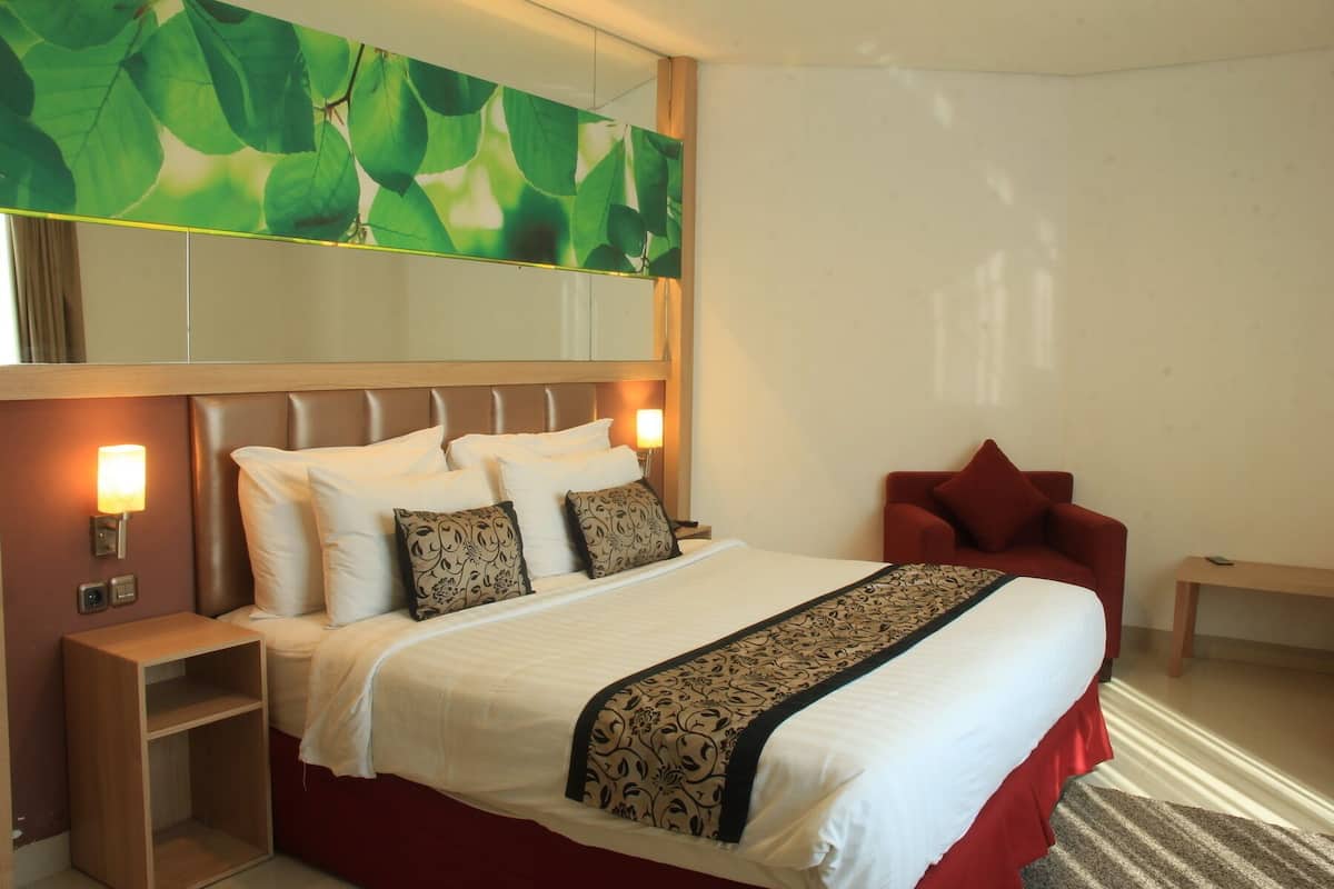 Een hotelkamer met een groot bed, een rode fauteuil, een houten nachtkastje en een spiegel aan de muur.