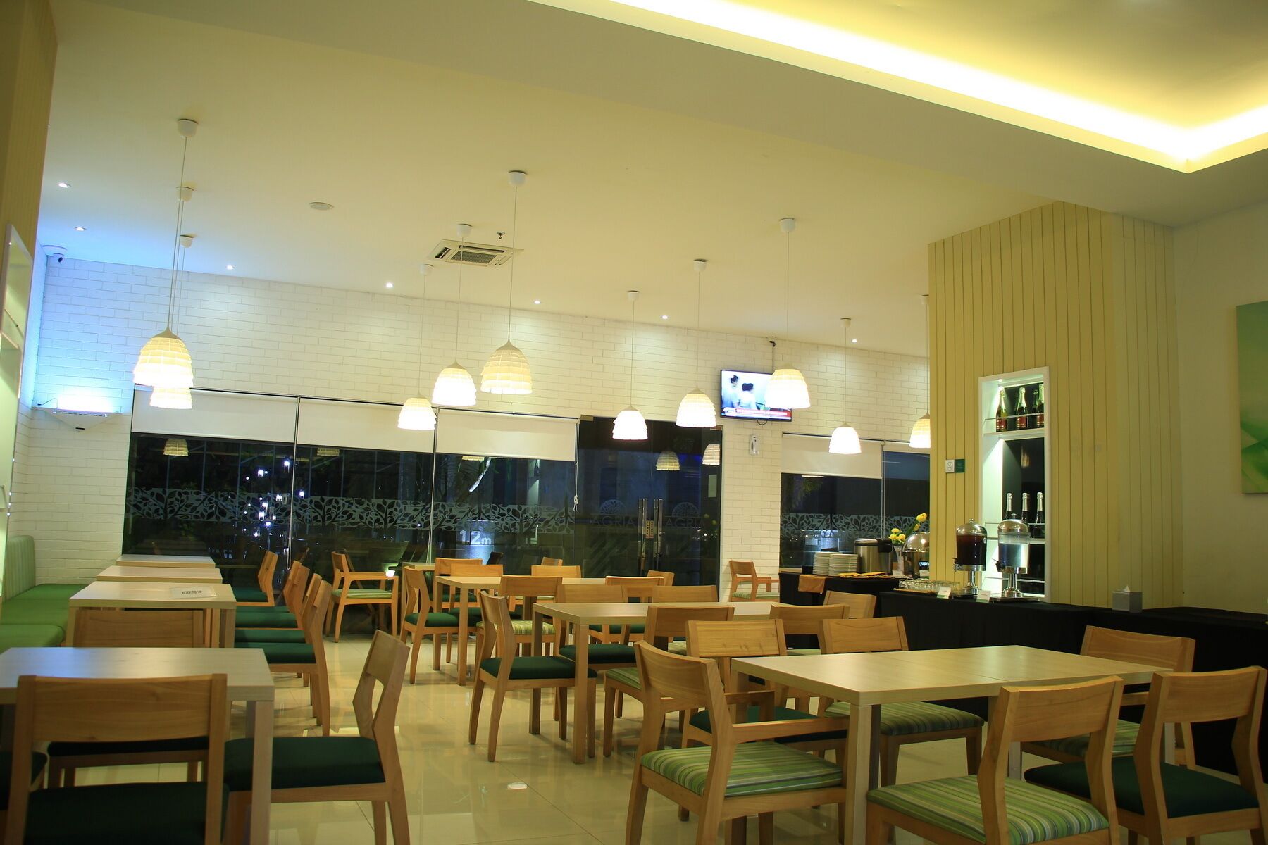 A restaurant with wooden tables and chairs, pendant lighting, a television, and a bar area.
