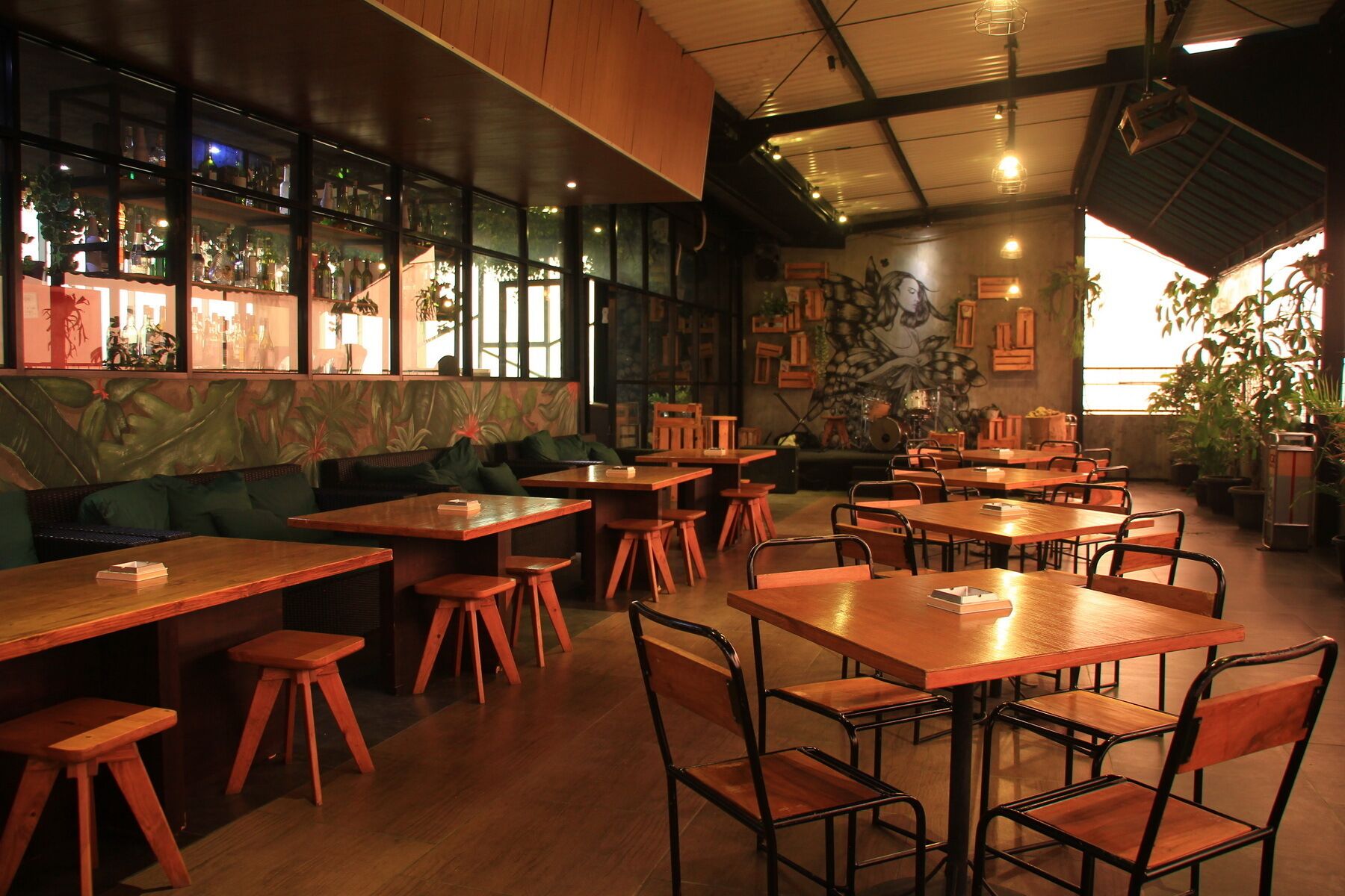 L’intérieur d’un restaurant présente des tables et des chaises en bois, un bar avec des bouteilles exposées et une fresque murale.