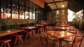 Interior de un restaurante con mesas y sillas de madera, una zona de bar con botellas y un mural en la pared.