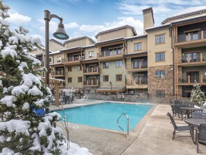 A multi-story hotel with a swimming pool, outdoor seating, and snow-covered trees.