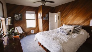 A bedroom with a wooden floor, a ceiling fan, a bed with white bedding, a chair, a small table with a plant, and a window with blinds. - Farmhouse right off of I-5 (Tangent)