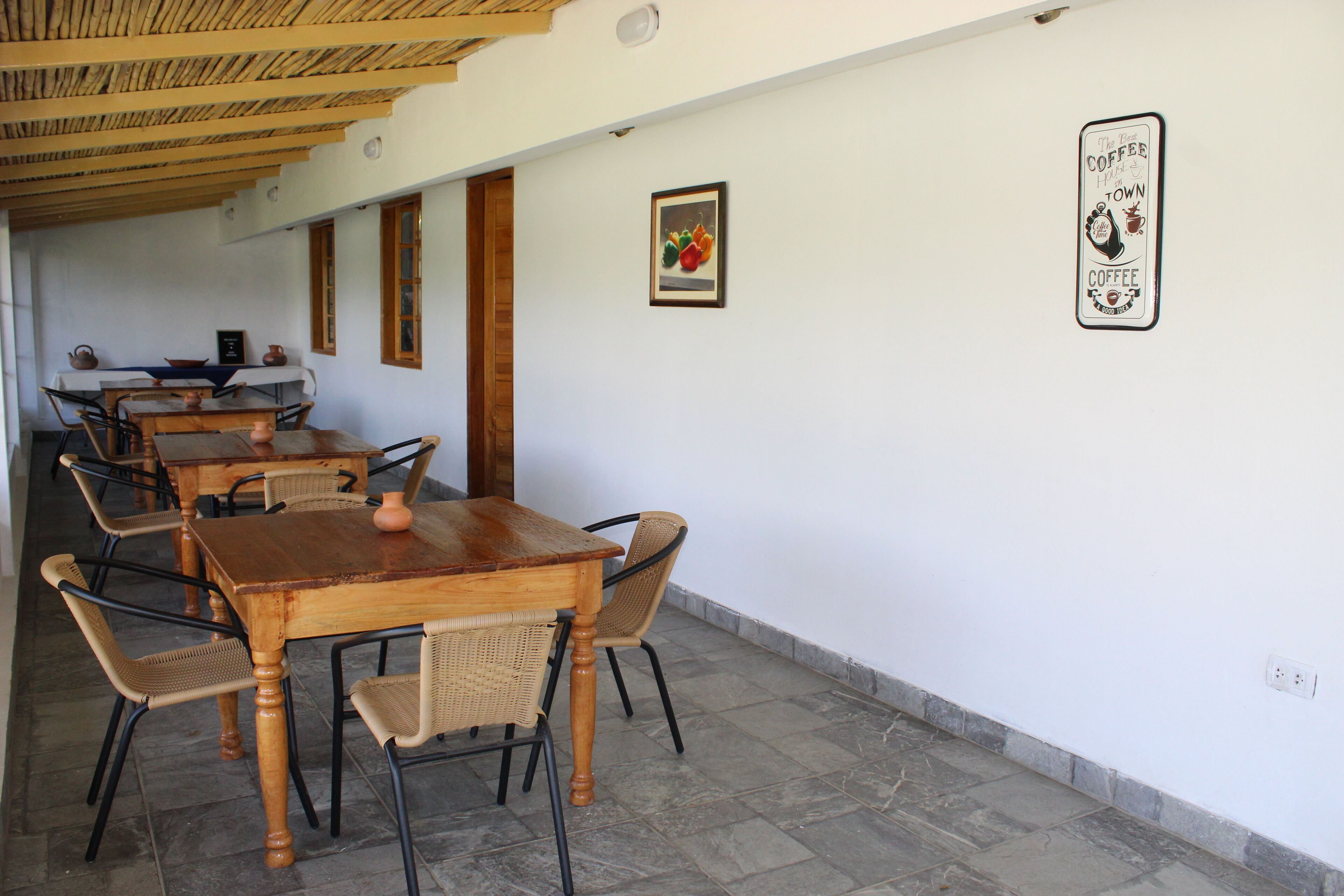 A dining area with wooden tables and wicker chairs, a tiled floor, and a wall with a framed picture and a sign.
