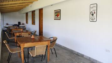 A dining area with wooden tables and wicker chairs, a tiled floor, and a wall with a framed picture and a sign.