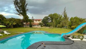 Une piscine avec un toboggan, entourée de chaises longues et d’une table ornée d’un vase.