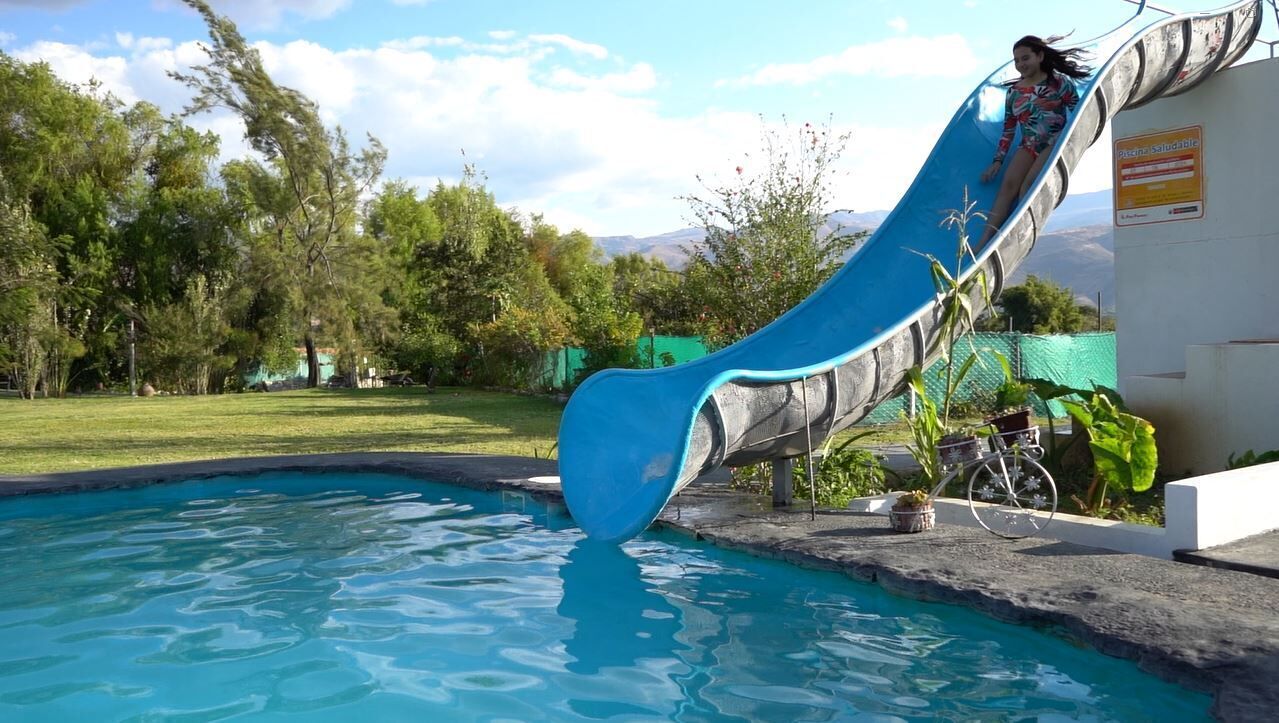 Uma piscina com um escorrega azul, rodeada por árvores e uma bicicleta.
