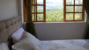 Une chambre à coucher avec un lit, une fenêtre avec des rideaux et une vue sur un paysage boisé.