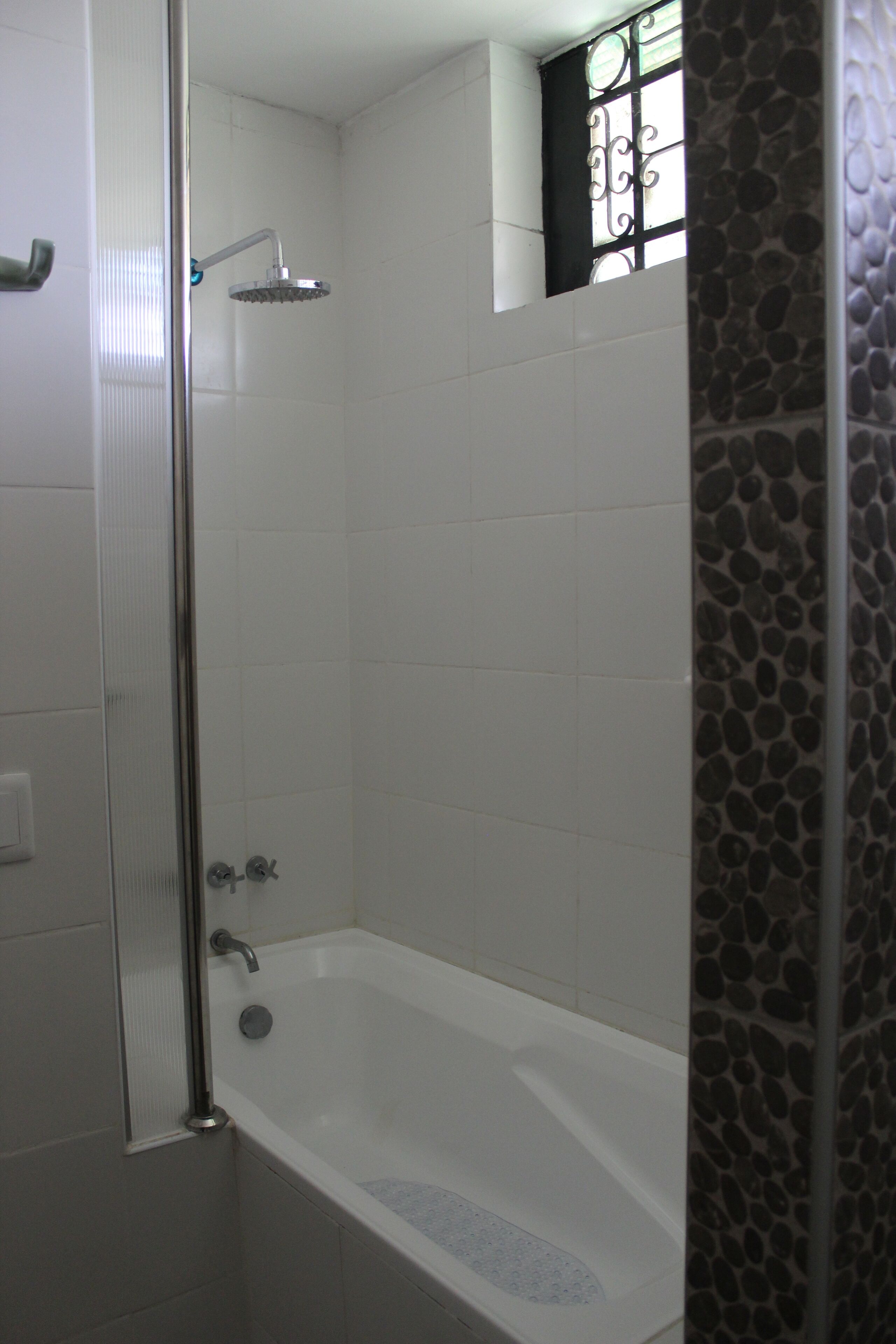 A bathroom with a shower, a bathtub, and a window with decorative bars.