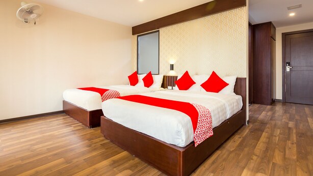 Une chambre d’hôtel avec un grand lit, une table de chevet, une commode, un miroir, un ventilateur fixé au mur et une porte.