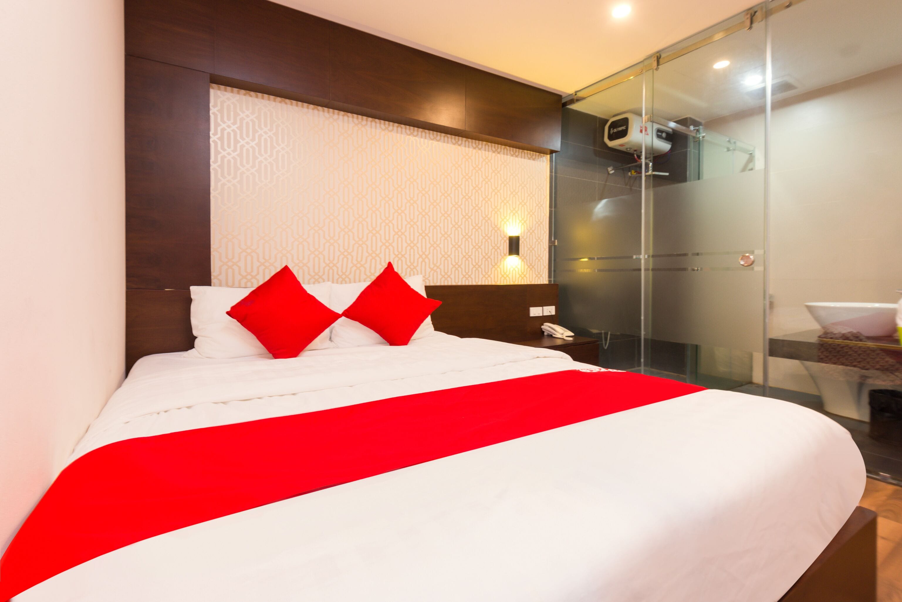 Una habitación de hotel con una cama, una mesita de noche, un teléfono y una cabina de ducha de vidrio.
