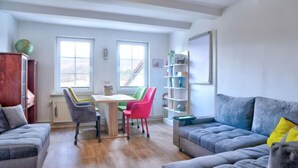 A modern living room with a grey sofa, a red chair, and a wooden cabinet. There is a table with papers and a lamp. - Phileas by Interhome (Schwalenberg)