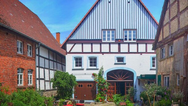 A traditional half-timbered building with a steep gable roof, a central entrance with a wooden door, and a small garden area with plants and a bench. - Phileas by Interhome (Schwalenberg)