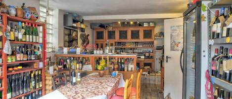 A restaurant with a long table, wooden chairs, and shelves filled with bottles.