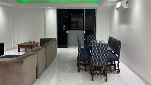 A modern living room with a sofa, dining table, and chairs. There is a TV, a small table, and a ceiling light. - BEACH FRONT CONDO WITH SPECTACULAR OCEAN VIEW OF THE ATLANTIC (guaruja)