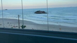 A beach view from a window with a clear sky, calm sea, and a distant island. - BEACH FRONT CONDO WITH SPECTACULAR OCEAN VIEW OF THE ATLANTIC (guaruja)