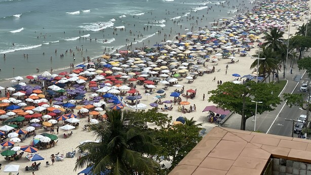 A crowded beach with numerous umbrellas and people. - BEACH FRONT CONDO WITH SPECTACULAR OCEAN VIEW OF THE ATLANTIC (guaruja)
