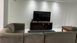 A modern living room with a flat-screen TV on a wooden stand, two sofas, and a small wooden table. - BEACH FRONT CONDO WITH SPECTACULAR OCEAN VIEW OF THE ATLANTIC (guaruja)