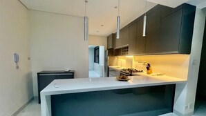 A modern kitchen with a central island, pendant lighting, and dark cabinetry. - BEACH FRONT CONDO WITH SPECTACULAR OCEAN VIEW OF THE ATLANTIC (guaruja)
