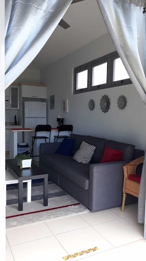 Una sala moderna con un sofá gris, una mesa de comedor y una cocina al fondo.