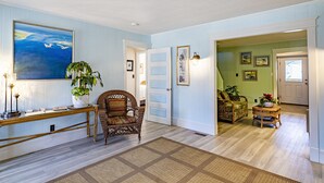 A spacious living room with a large painting, a potted plant, and a wicker chair. - Island Guesthouse and Motel (Manteo)