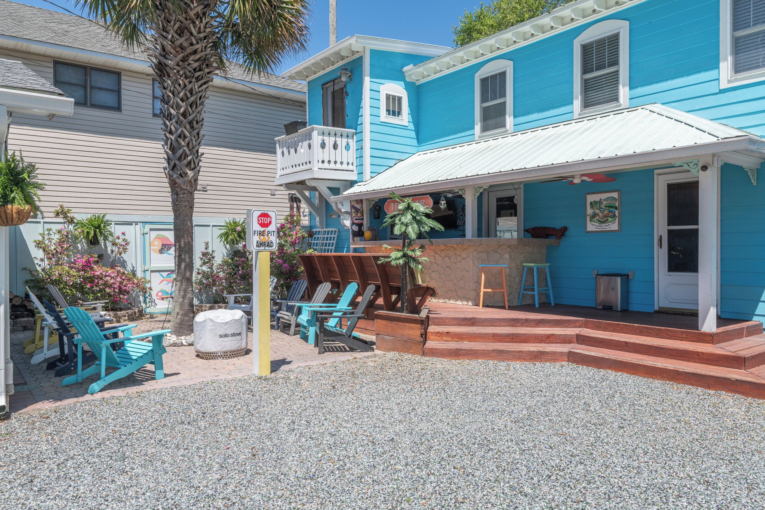 Un bâtiment situé sur la côte, avec une façade bleue, un balcon, des sièges à l’extérieur et une terrasse en gravier.
