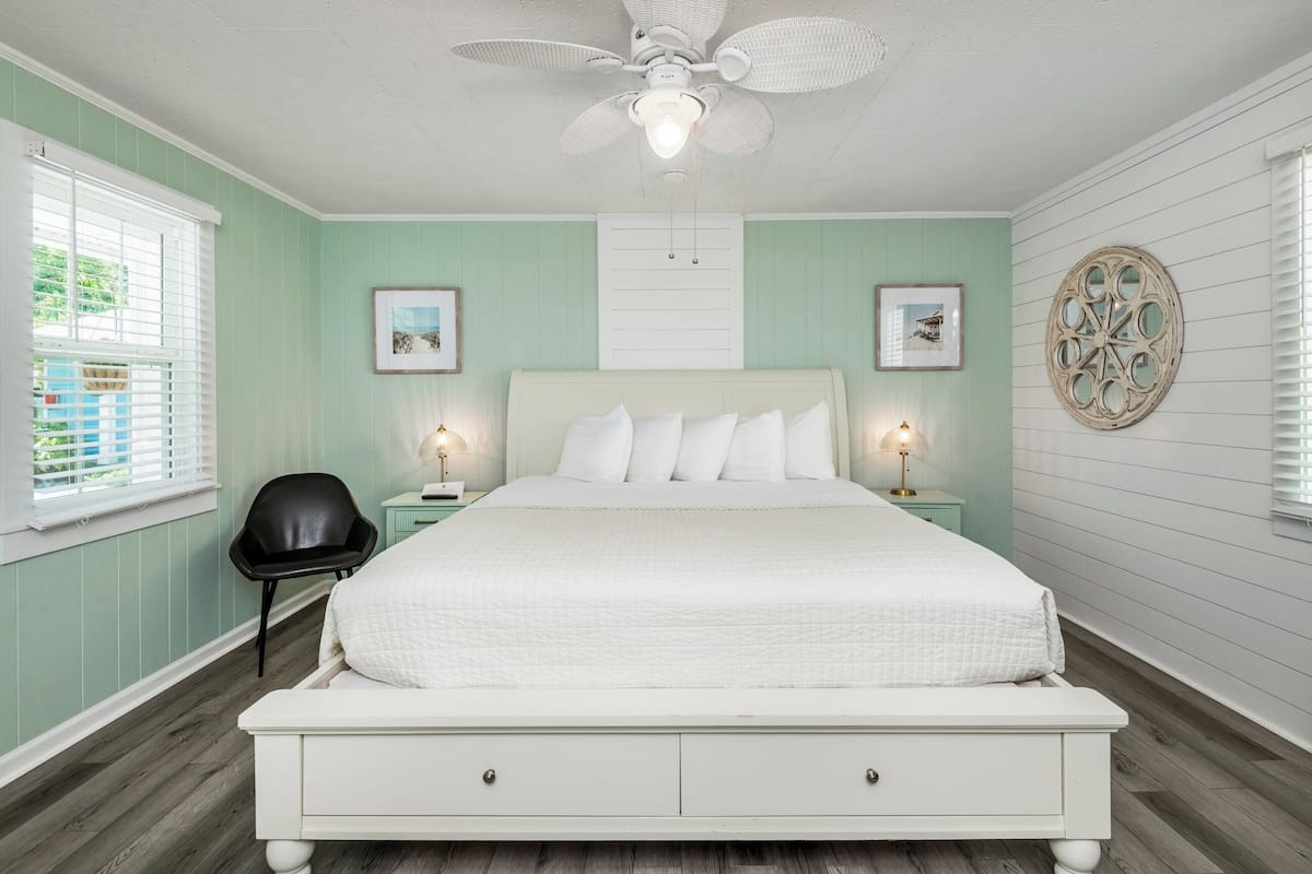 Une chambre à coucher avec un grand lit, deux tables de chevet avec des lampes, un ventilateur de plafond et un élément décoratif mural.