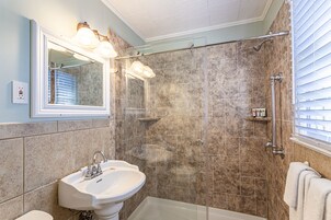Un baño con lavamanos pedestal, cabina de ducha y un espejo grande con iluminación.