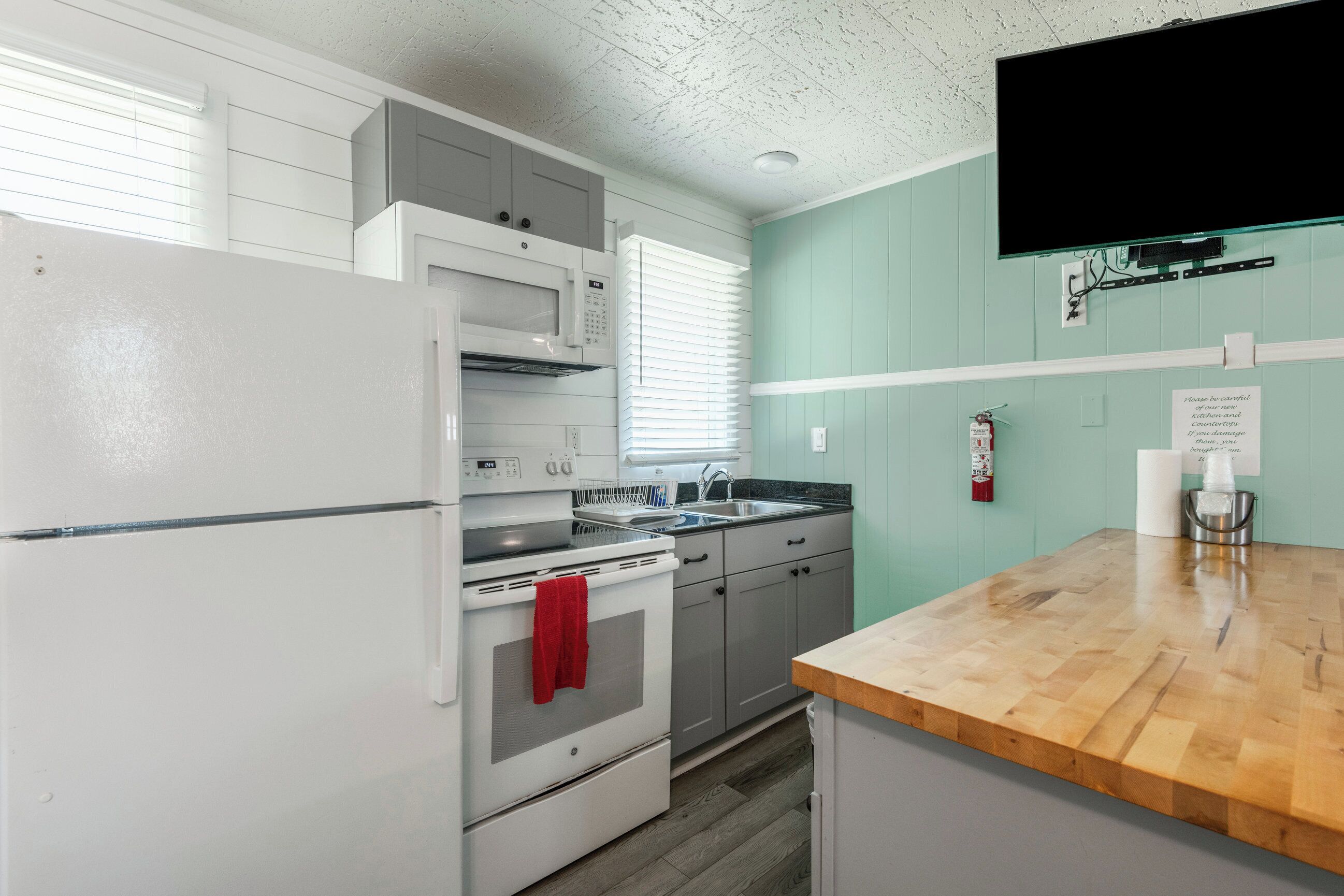 A kitchen with white appliances, a wooden countertop, and a teal wall.
