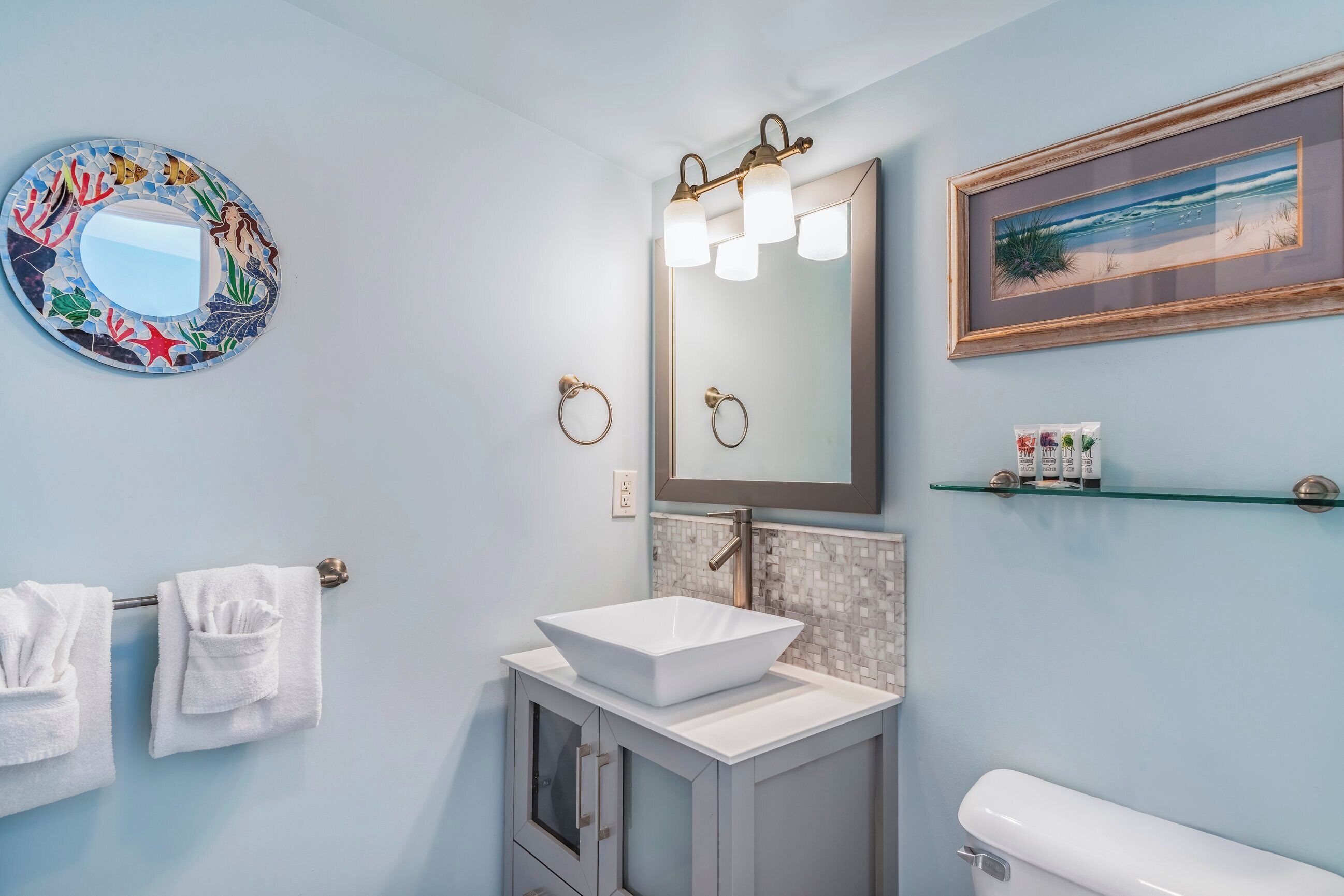 Ein Badezimmer mit einem weißen Waschbecken, einem Spiegel und einem gerahmten Bild an der Wand.