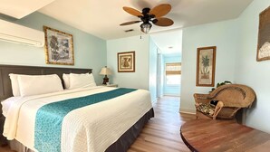 A bedroom with a bed, a ceiling fan, a wooden floor, and a view to another room. - Island Guesthouse and Motel (Manteo)